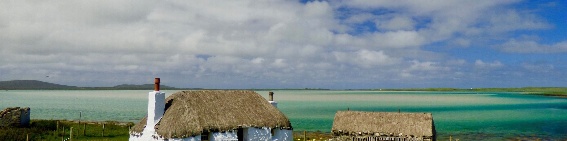 The restored Cottages of Struan near Malacleit are a beautiful example of traditional life on the Isle of North Uist, the clear waters of the bay shown the underlying white sands and the Isle of Vallay in the distance.