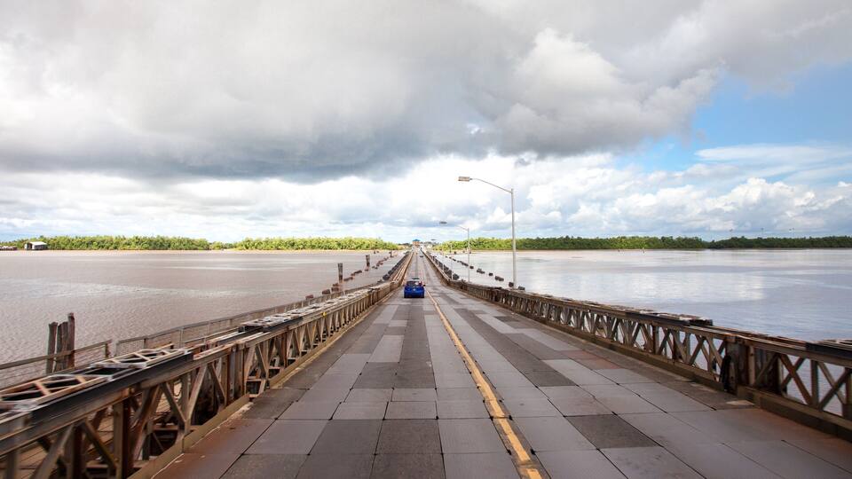 A long wooden bridge over a calm river with a cloudy sky.