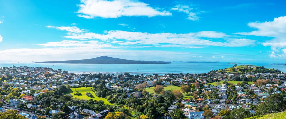 Une ville côtière avec une montagne qui se profile à l’horizon, entourée de verdure et de maisons.