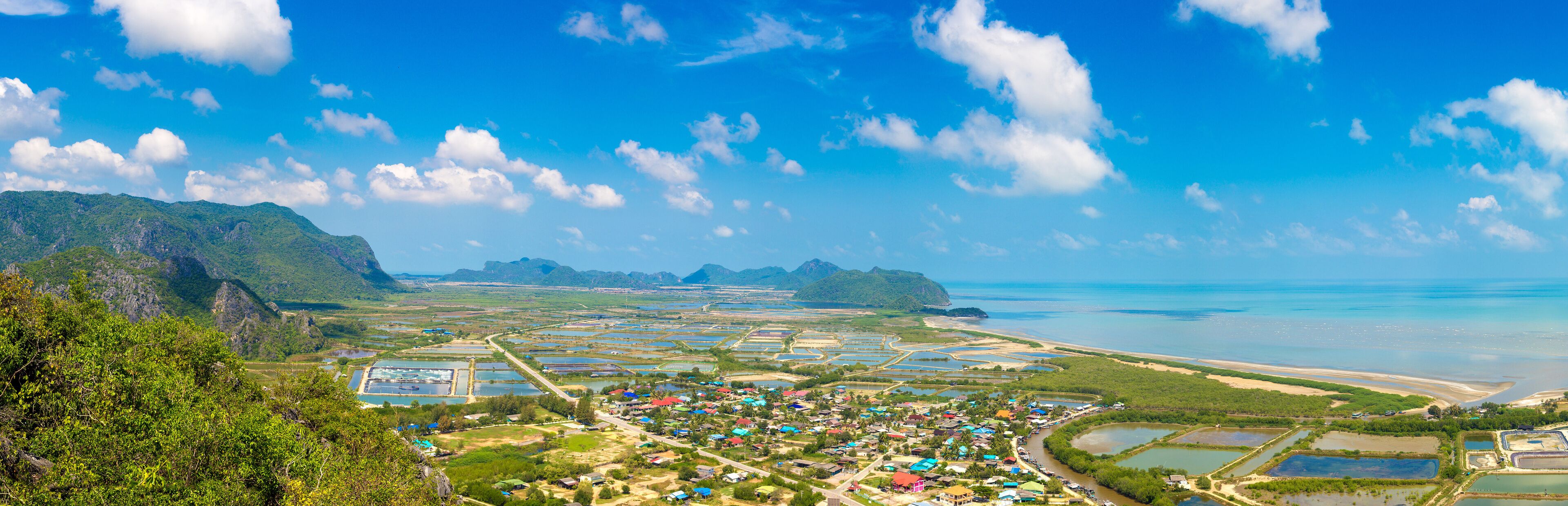 A coastal town with a mix of residential and industrial areas, surrounded by mountains and a clear blue sky.