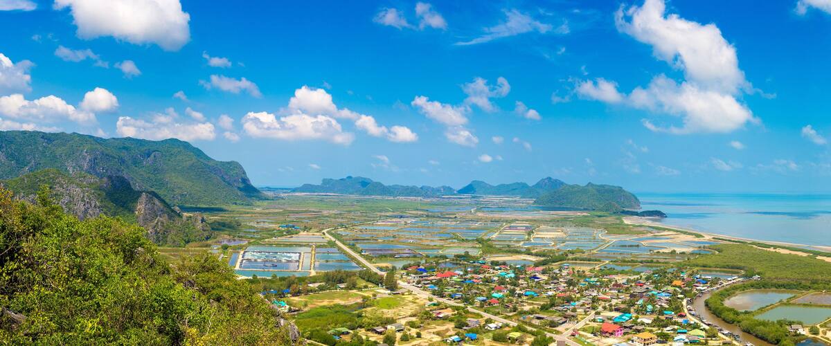 A coastal town with a mix of residential and industrial areas, surrounded by mountains and a clear blue sky.