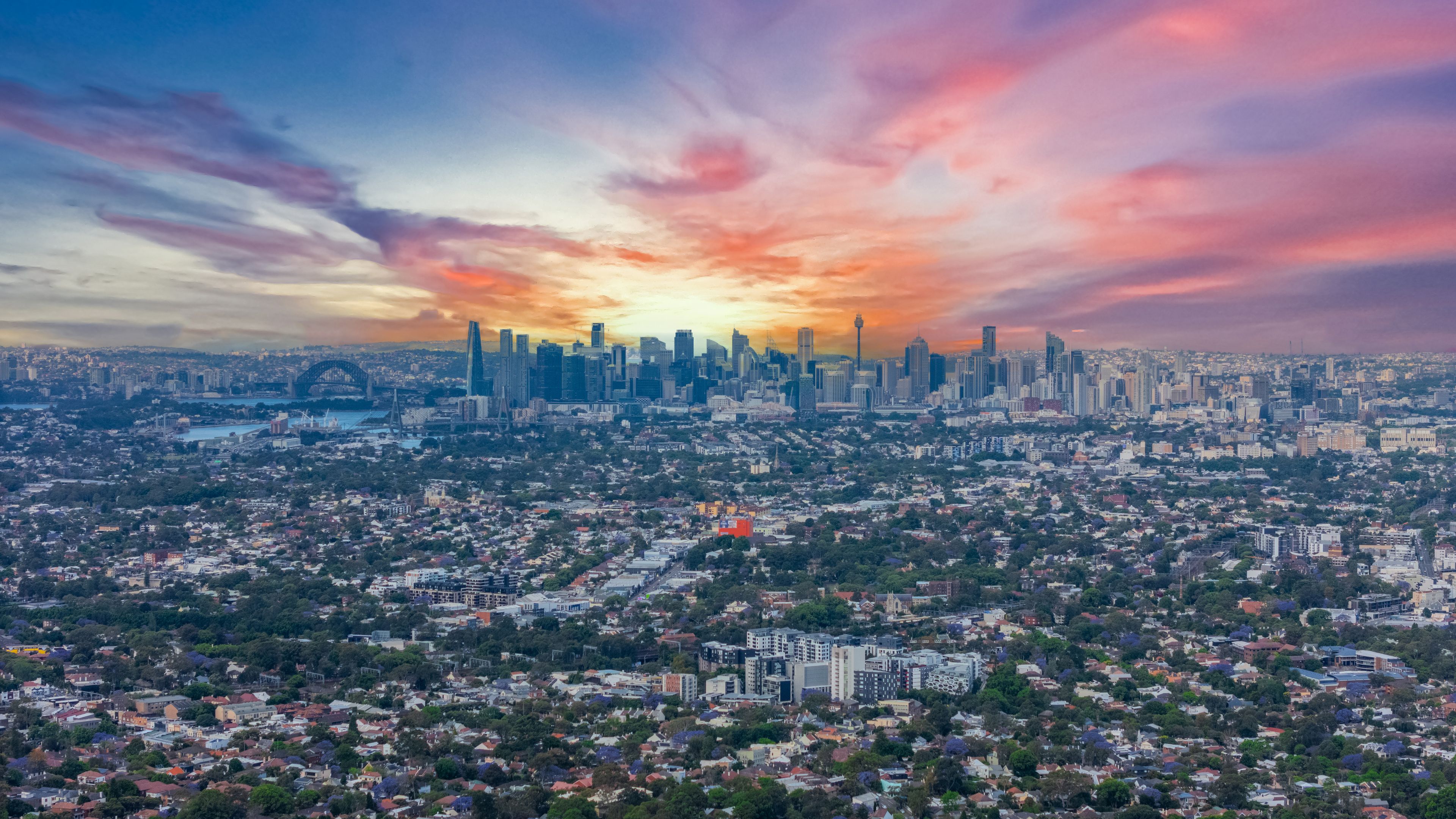 A city skyline with a sunset, featuring prominent skyscrapers and a dense residential area.