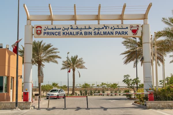 The entrance to Prince Khalifa Bin Salman Park with palm trees and a car in the foreground.