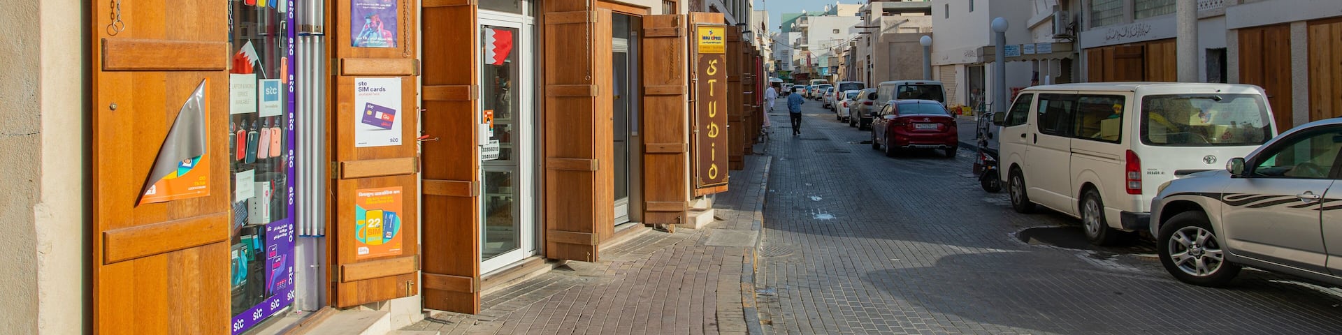A narrow street lined with shops and parked cars.