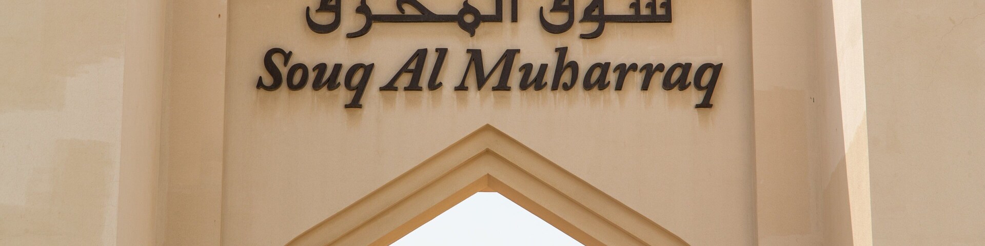 Un arco de entrada con el letrero "Souq Al Muharraq" en árabe e inglés.