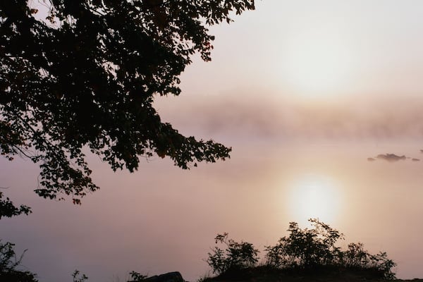 This is Squam Lake surrounded by a morning fog in autumn. There are trees surrounding the lake.