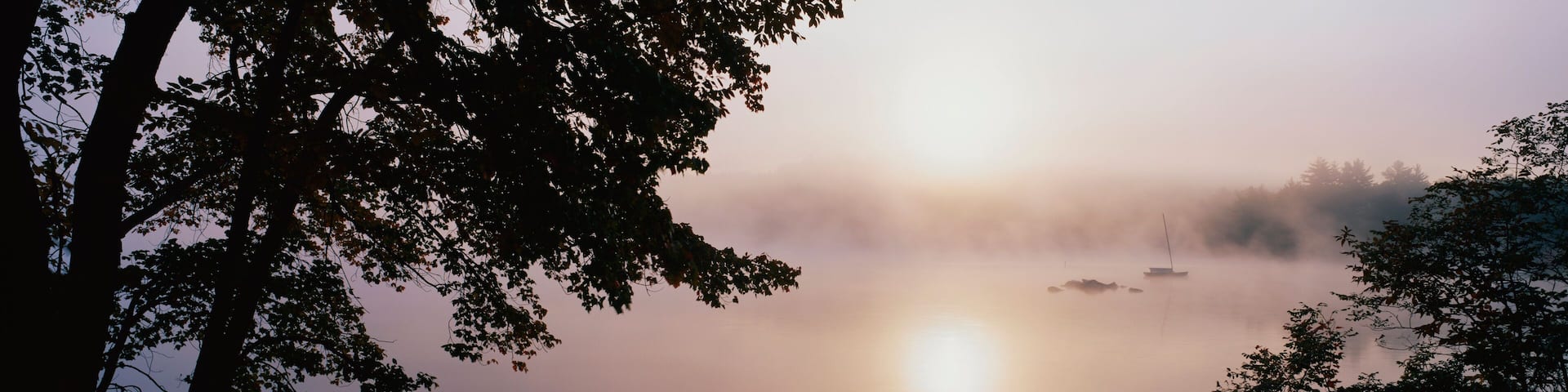 This is Squam Lake surrounded by a morning fog in autumn. There are trees surrounding the lake.