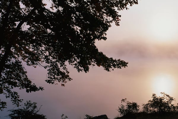 This is Squam Lake surrounded by a morning fog in autumn. There are trees surrounding the lake.