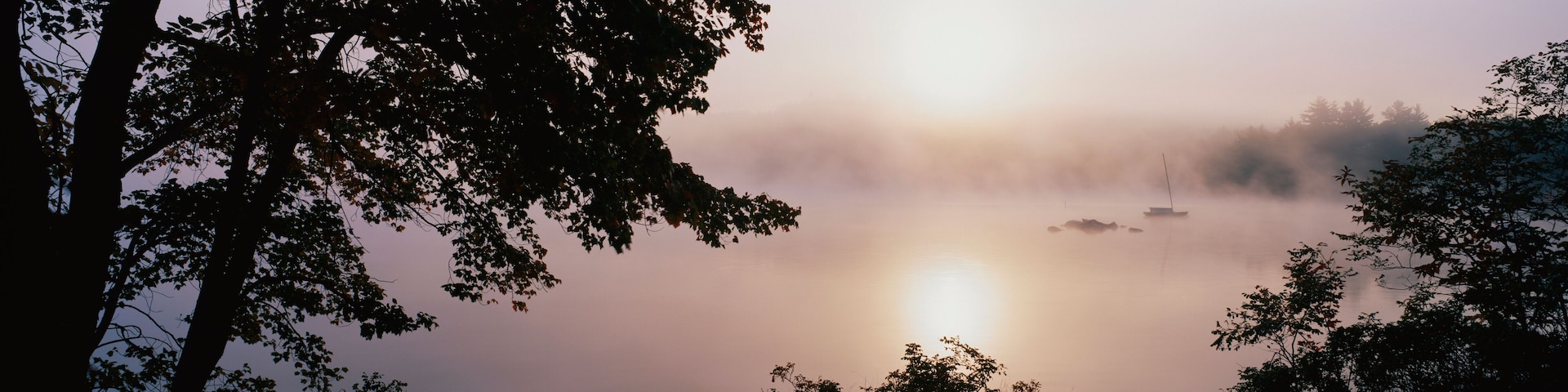 This is Squam Lake surrounded by a morning fog in autumn. There are trees surrounding the lake.