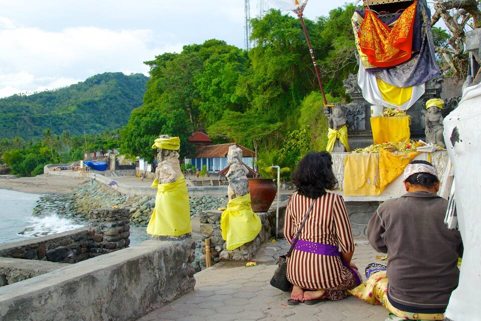 A coastal temple with statues, a stone wall, and a beach in the background.