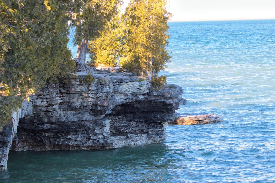 A rocky cliff with trees, overlooking a calm body of water.