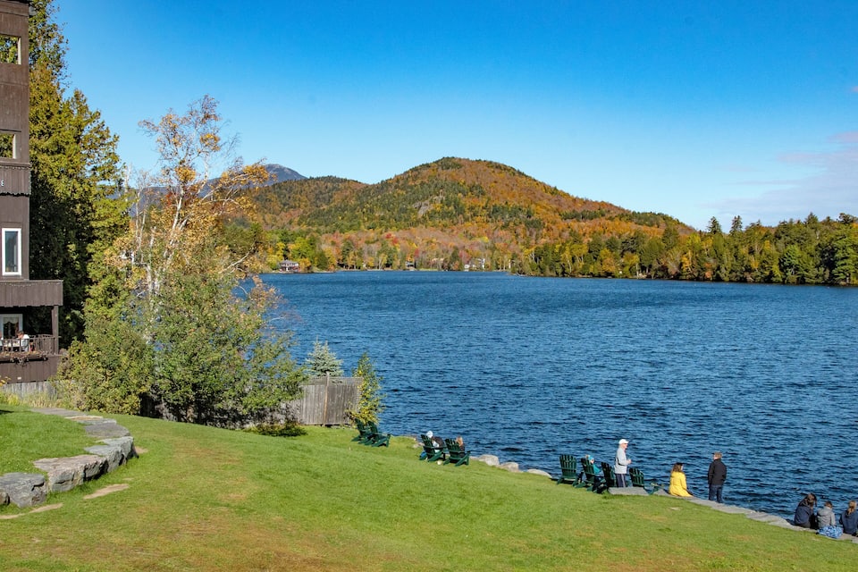 A lake with a wooden dock, a grassy area, and autumn-colored trees.