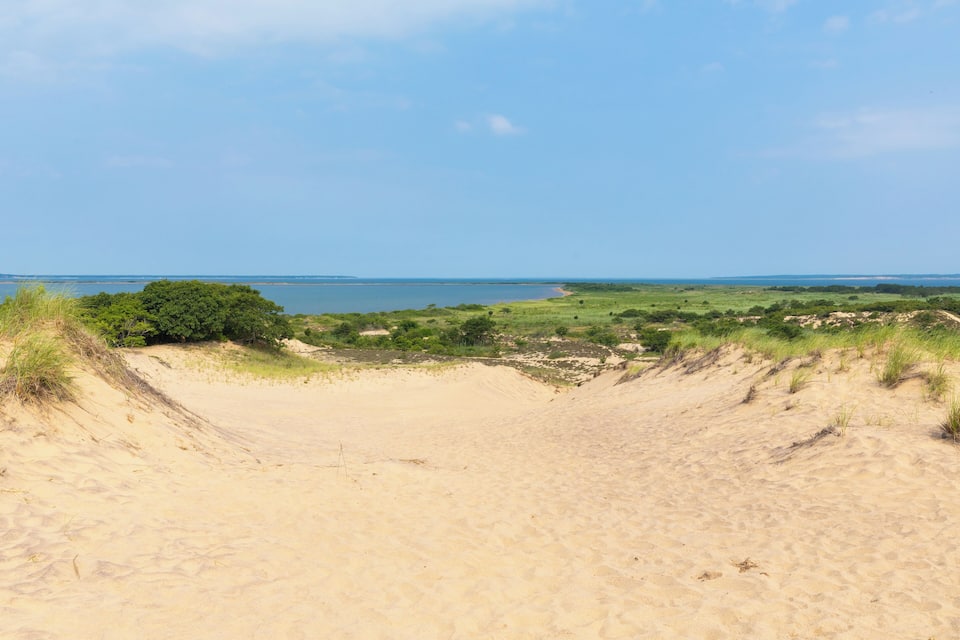 Een kustlandschap met duinen, een strand en een veraf gelegen wateroppervlak.