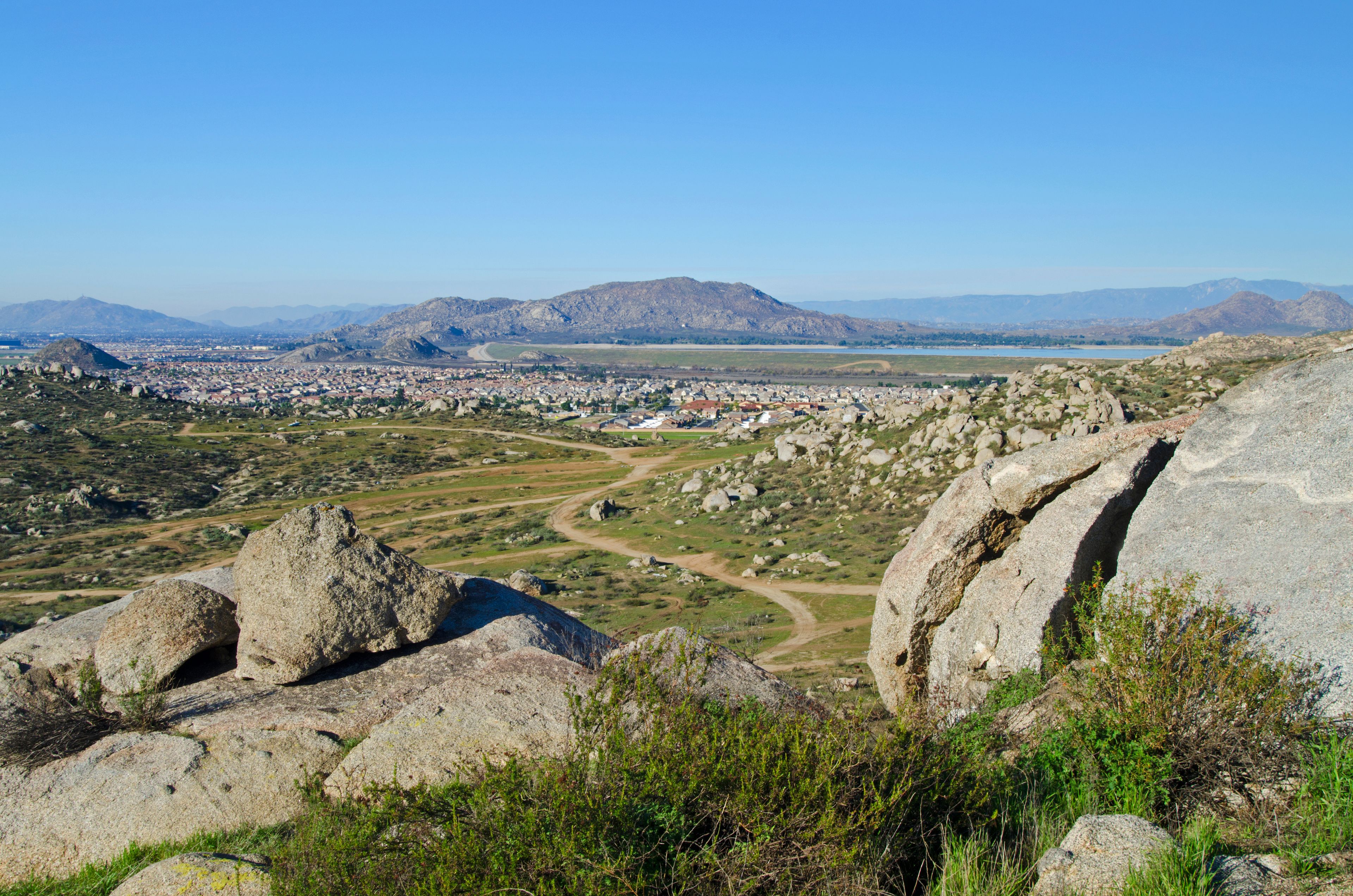 A mountainous landscape with a town in the valley, a winding road, and a large body of water in the distance.