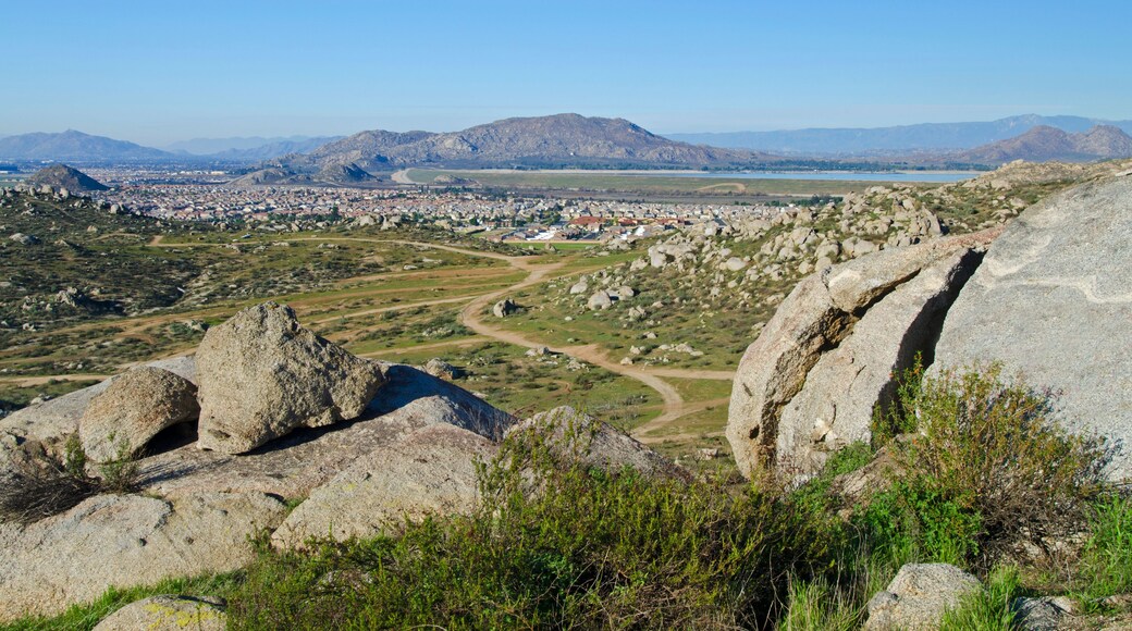 A mountainous landscape with a town in the valley, a winding road, and a large body of water in the distance.