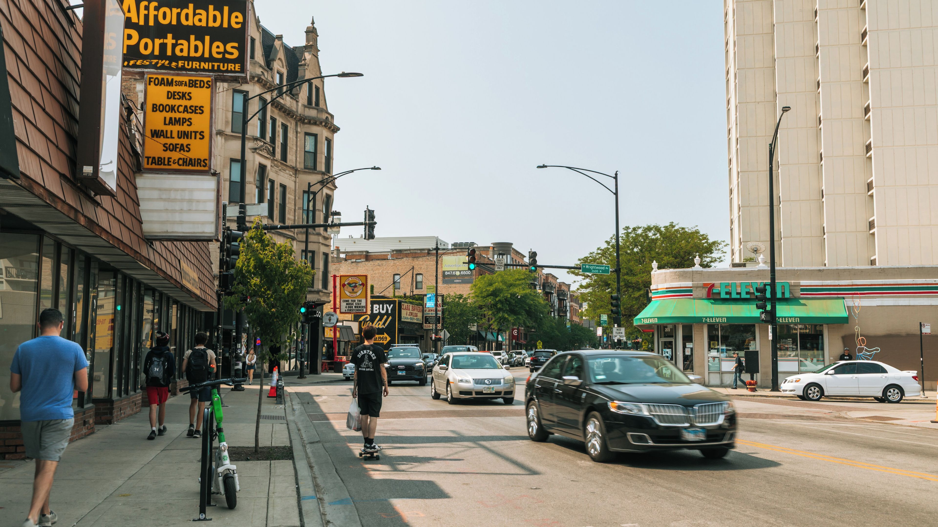 A busy urban street with various storefronts, including a furniture store and a 7-Eleven.
