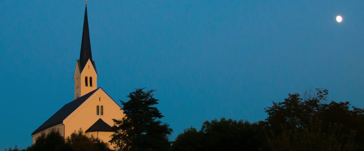 A church with a tall steeple and a moon in the sky.