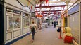 A covered market with shops on either side, a large decorative vase, and a person walking.