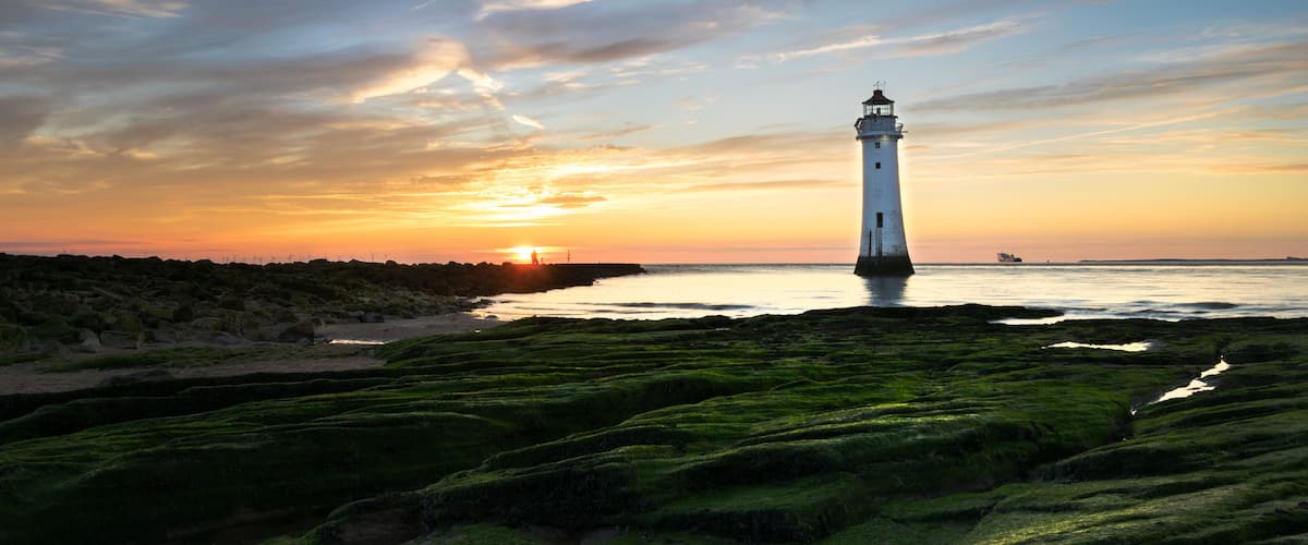 A lighthouse at sunset with a clear sky and green moss-covered ground.