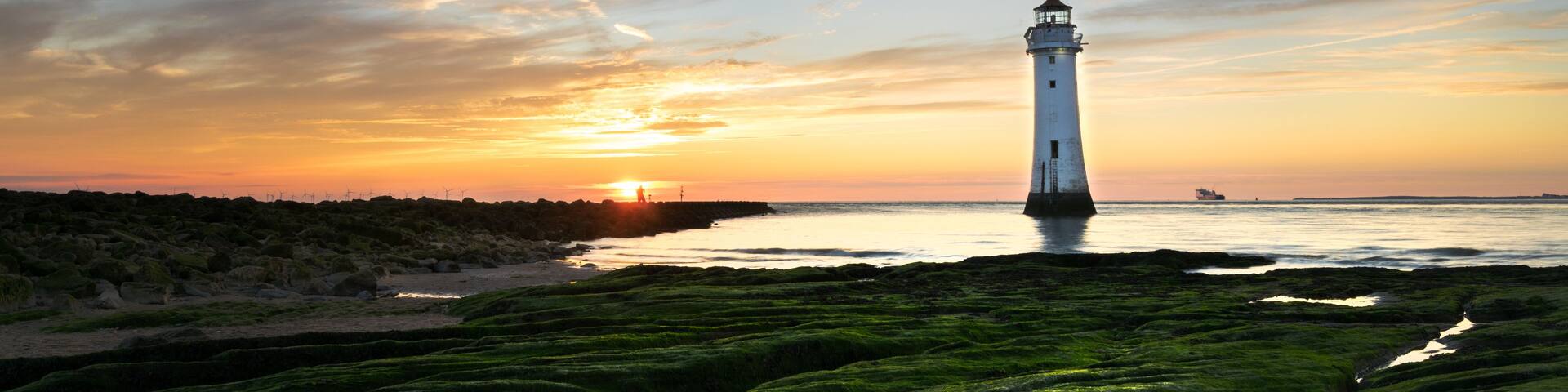 A lighthouse at sunset with a clear sky and green moss-covered ground.