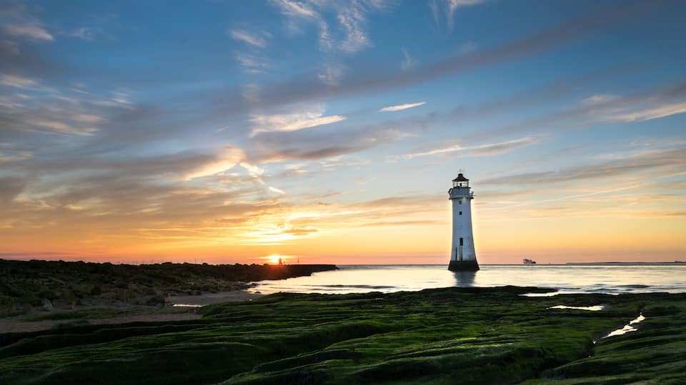 A lighthouse at sunset with a clear sky and green moss-covered ground.