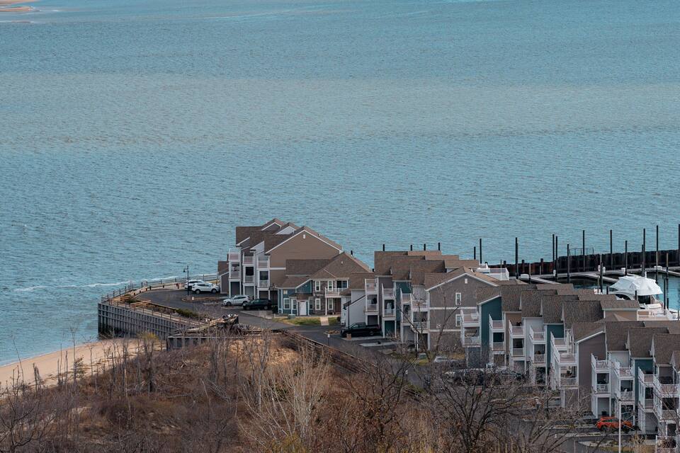 A coastal residential area with buildings near the shore and a distant bridge.
