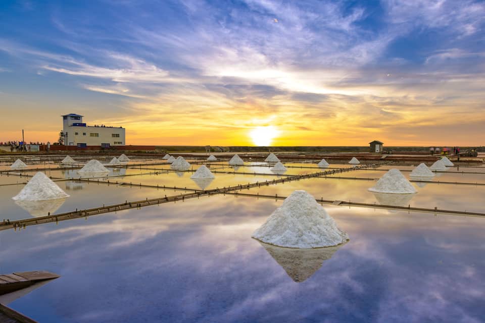 A salt flat with white salt formations and a building in the background during sunset.