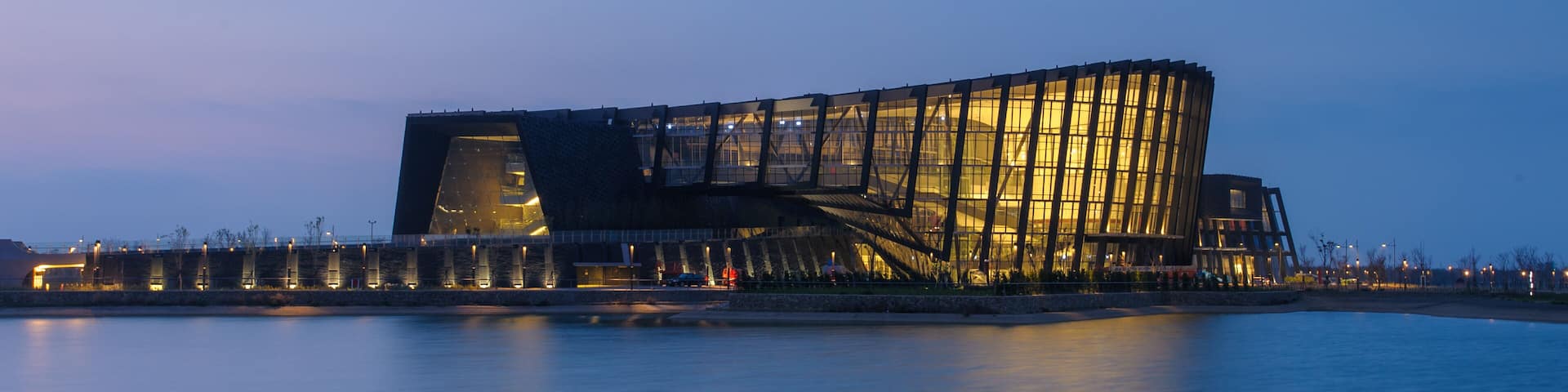 A modern architectural building with a unique curved design, situated by a calm body of water.