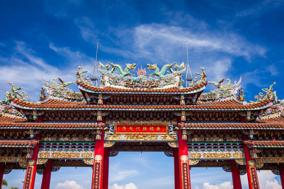 Um portão tradicional chinês com elaboradas decorações de dragão e um arco vermelho.