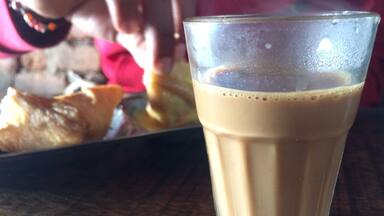 A glass of iced coffee on a wooden table with a blurred background of a person and food.