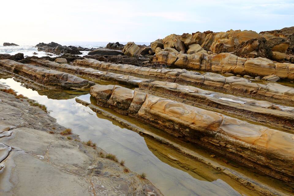 Layered rock formations with water pools at a coastal location.