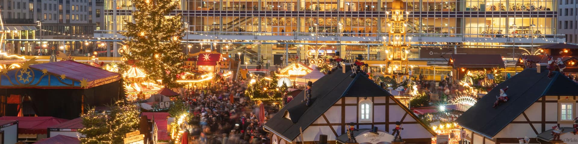 Un mercado festivo con un gran árbol de Navidad, edificios tradicionales y una imponente aguja de iglesia.