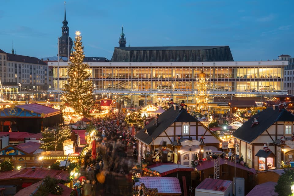 A festive market with a large Christmas tree, traditional buildings, and a prominent church spire.