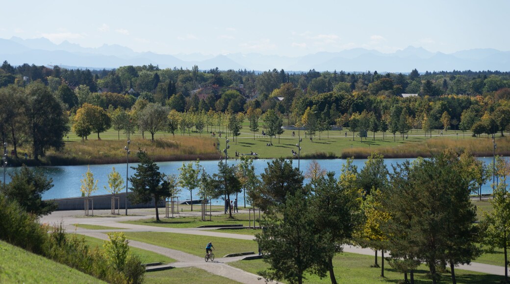 Beautiful panoramic landscape with a lake and trees in the green "Riemer Park" in summer, aerial view from a hillock, in the back the Bavarian mountains Alps, blue sky.