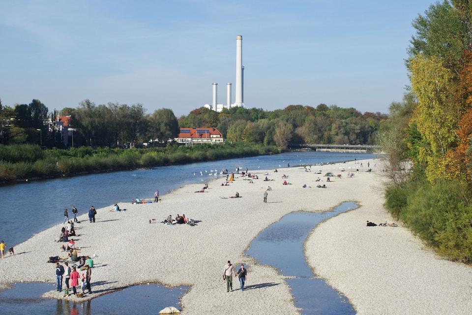 A riverside beach with people sunbathing and walking.