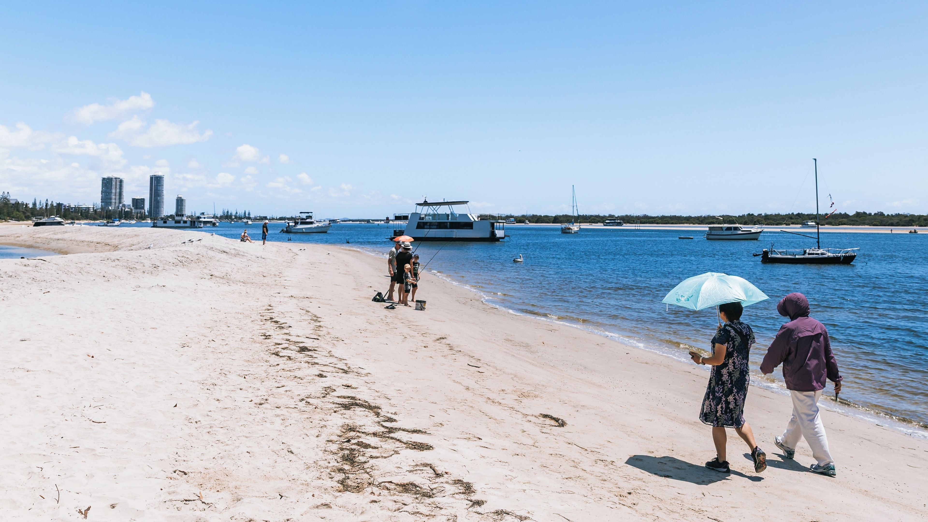A sandy beach with boats in the water and a city skyline in the background.