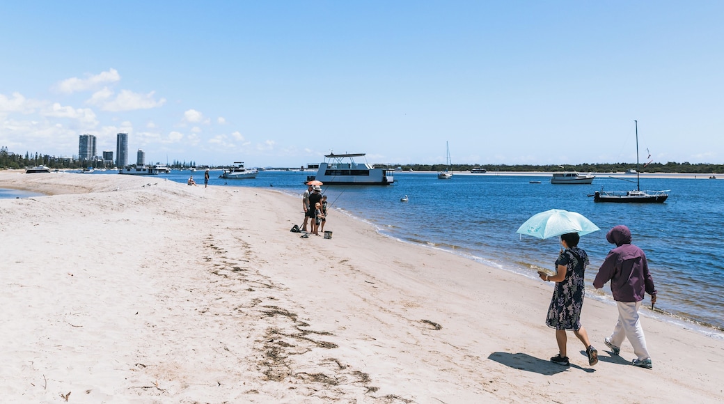 A sandy beach with boats in the water and a city skyline in the background.