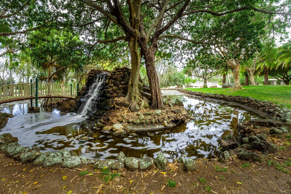 A pond with a waterfall, surrounded by trees and a stone bridge.