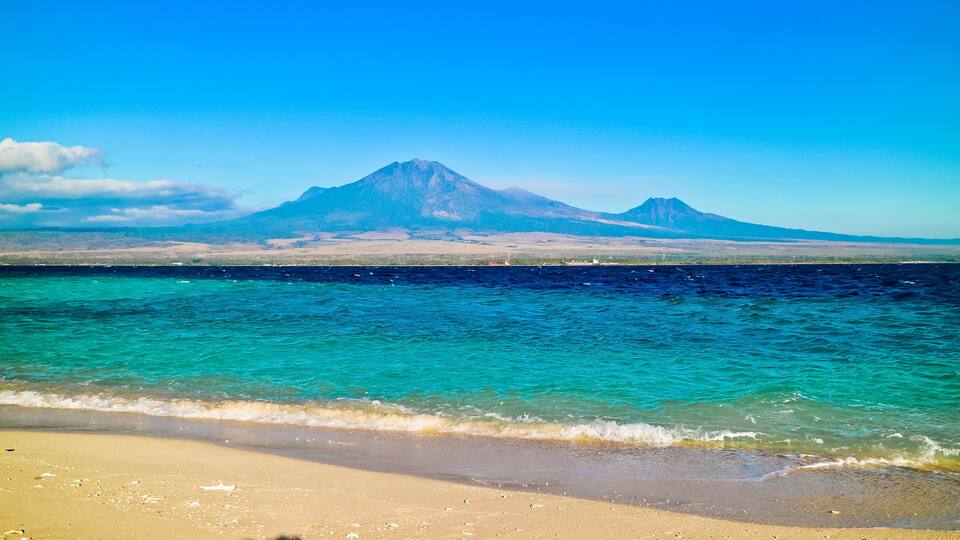 A beach with clear turquoise waters and a mountain in the background.