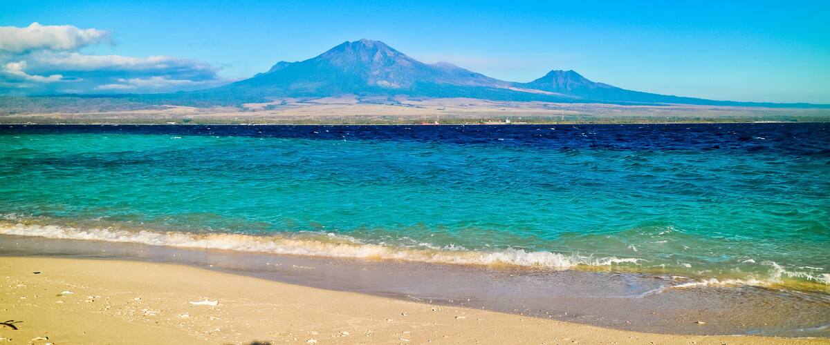 A beach with clear turquoise waters and a mountain in the background.