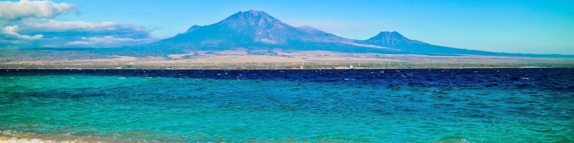 A beach with clear turquoise waters and a mountain in the background.