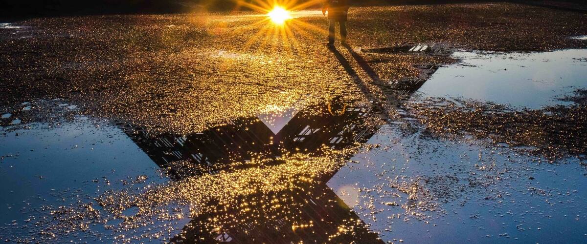 A large metal structure with a star-like shape, reflecting the sunset over a body of water.