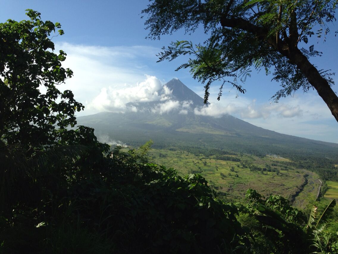 A mountain with a cloud-covered peak, surrounded by lush green vegetation and a clear sky.