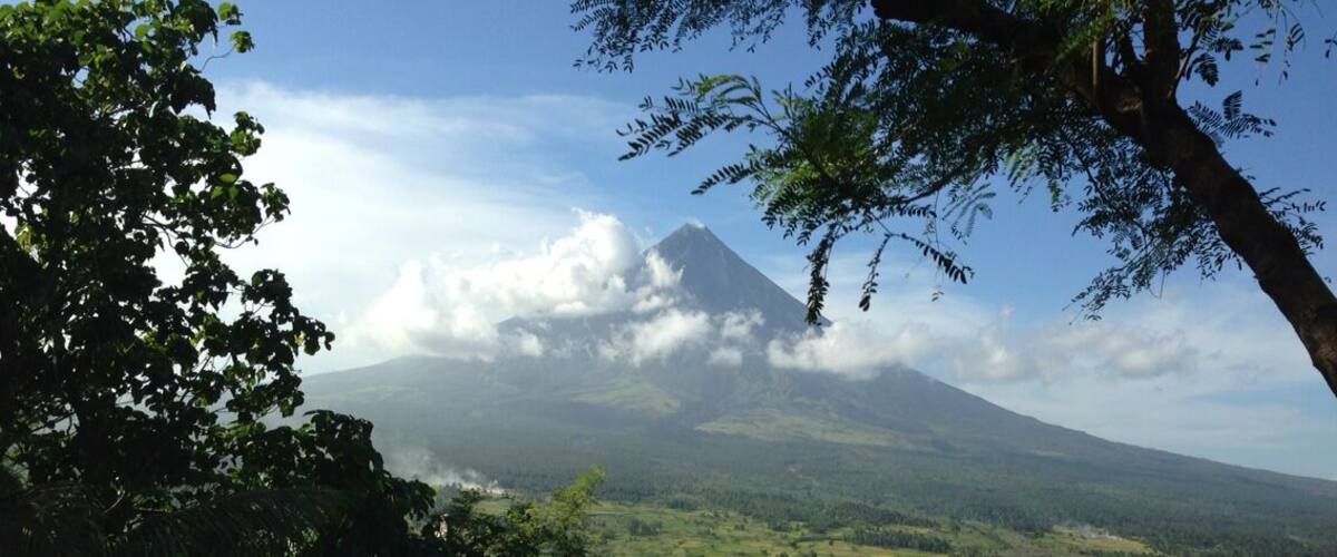 A mountain with a cloud-covered peak, surrounded by lush green vegetation and a clear sky.