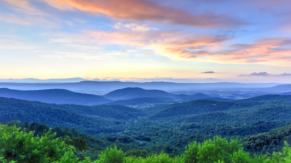 A mountainous landscape with dense forests and a colorful sky.