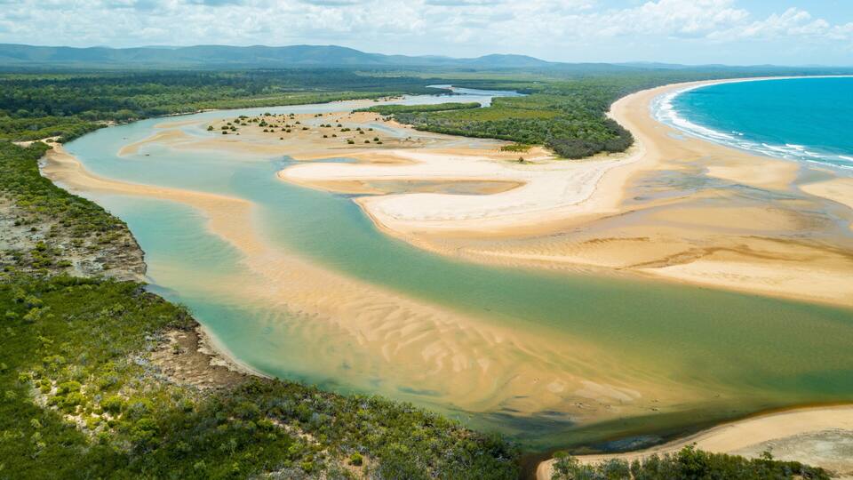 A coastal landscape with a sandy beach, clear blue waters, and a river meandering through a green forest.