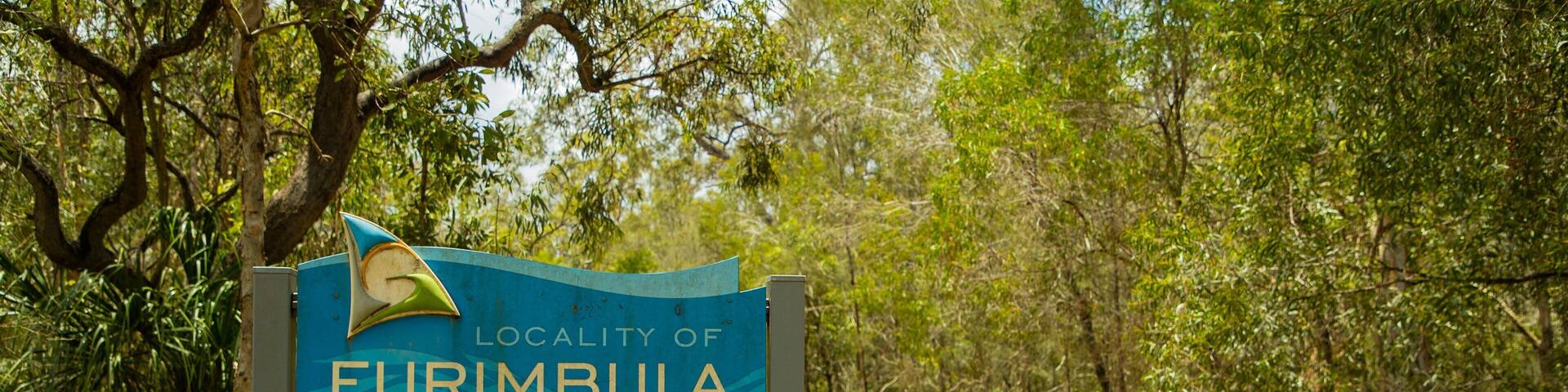 A sign for the locality of Eurimblia with a wooden fence and trees in the background.