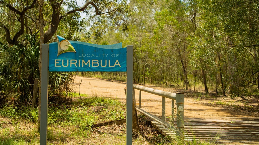 A sign for the locality of Eurimblia with a wooden fence and trees in the background.