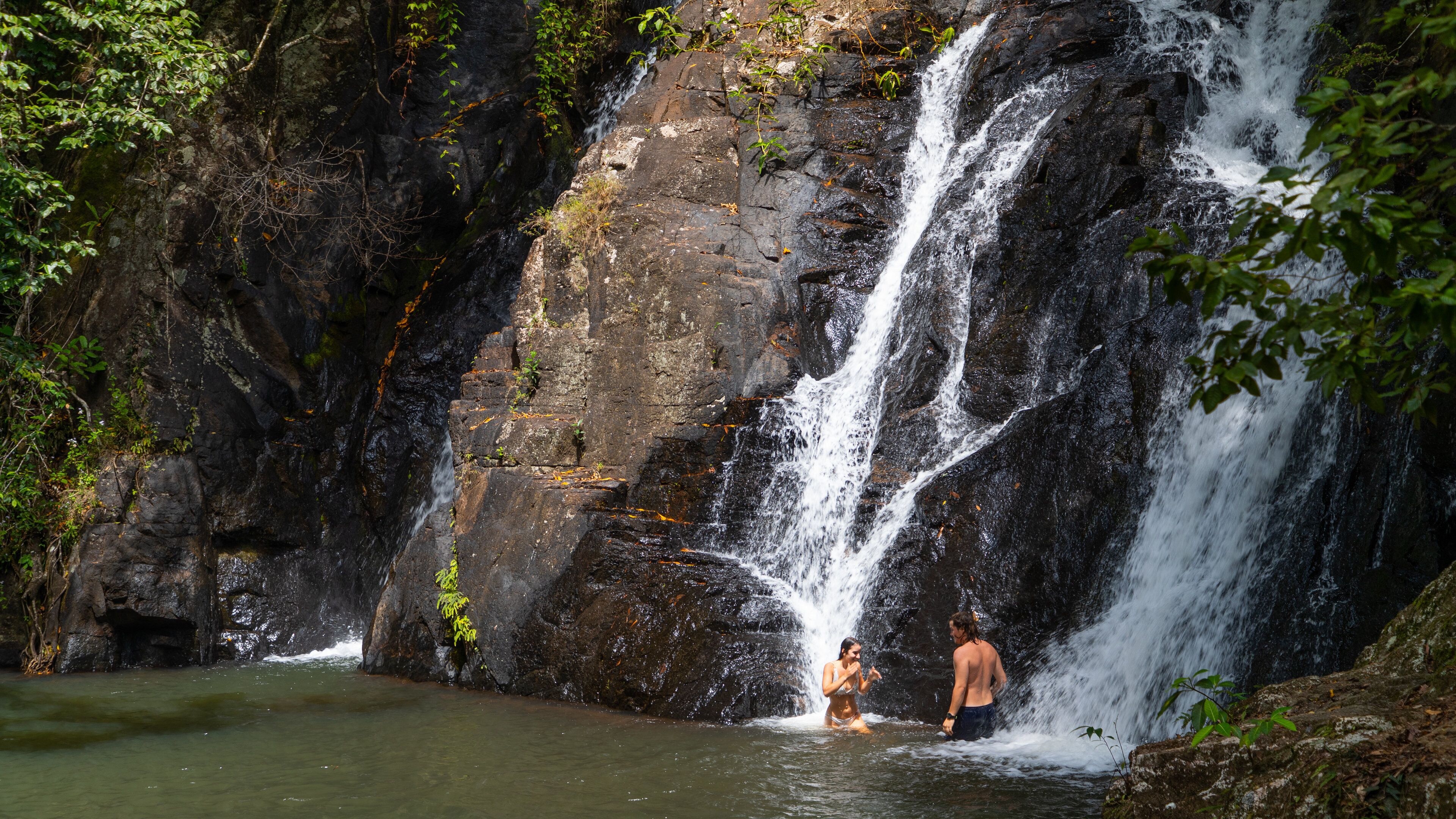 A waterfall in a forested area with a person standing in the water.