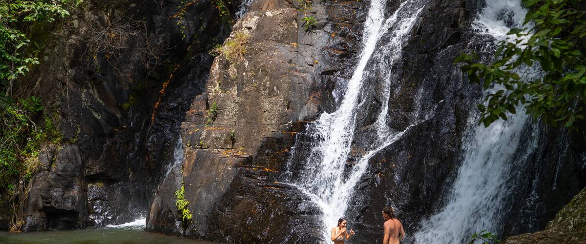 A waterfall in a forested area with a person standing in the water.
